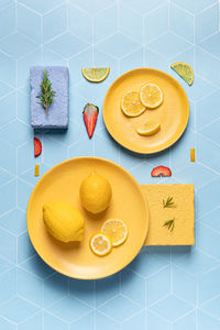 Top view flat lay composition of sour lemon on bright plates with slices of strawberry and rosemary twigs on sponges