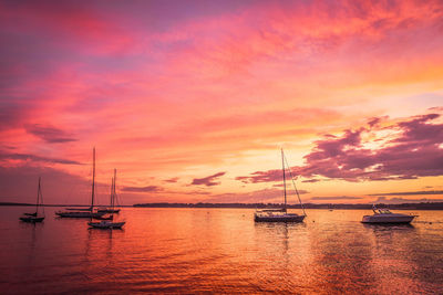 Sailboats moored on sea against sky during sunset