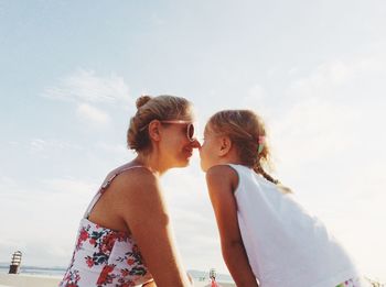 Mother and daughter sitting against sea at beach