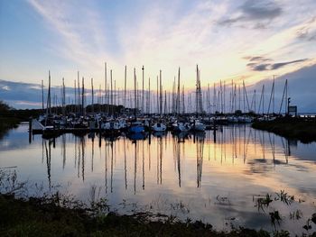 Sailboats moored in harbor at sunset