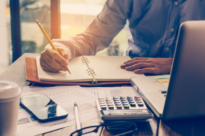 Midsection of man writing on diary at desk