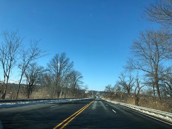 Road amidst bare trees against clear blue sky