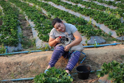 Portrait of smiling woman feeding strawberry to puppy while sitting in farm