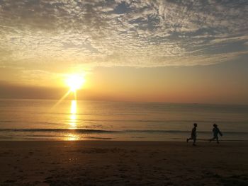 Silhouette people on beach against sky during sunset