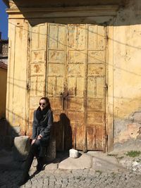 Young woman wearing sunglasses while sitting against old door