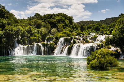 Scenic view of waterfall in forest against sky