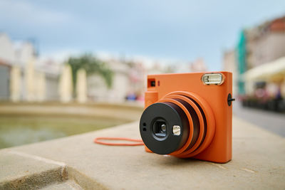 Vintage orange instant camera in city with cloudy sky. travel shooting equipment