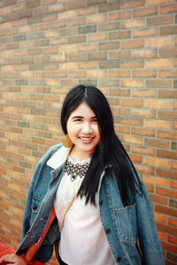 Portrait of smiling young woman standing against brick wall