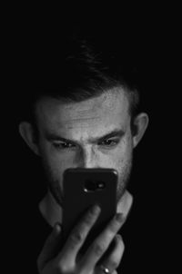 Close-up portrait of mid adult man using mobile phone against black background