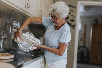 Senior woman standing over kitchen sink and pouring water out of saucepan