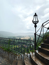 Street light by railing against sky during rainy season