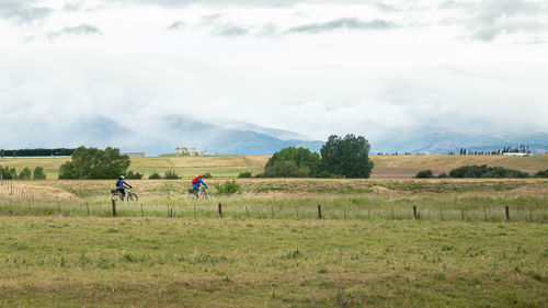 People riding motorcycle on field against sky