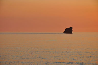 Silhouette rock in sea against sky during sunset