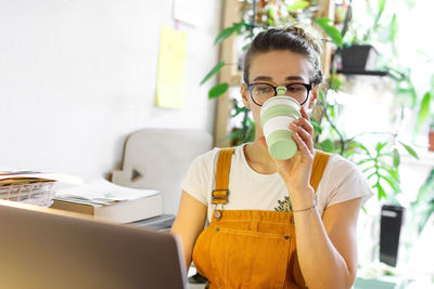 Woman drinking coffee while using laptop at home