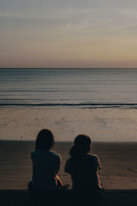 Rear view of people sitting on beach during sunset