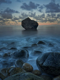 Rocks in sea against sky during sunset