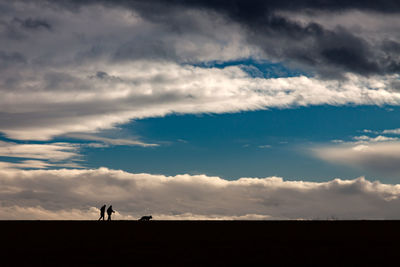 Silhouette people on land against sky during sunset