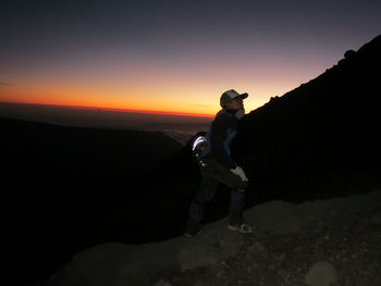 Full length of man standing on rock against sky during sunset