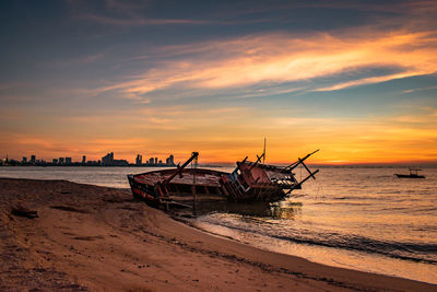 Fishing boat on beach against sky during sunset