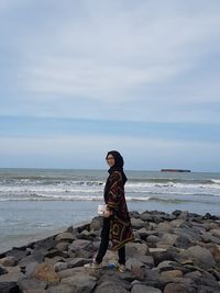 Rear view of woman standing on beach against sky