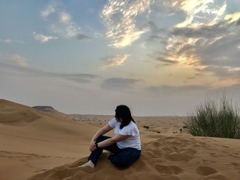 Full length of man sitting on sand at beach against sky