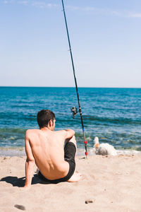 Rear view of shirtless man on beach against sky