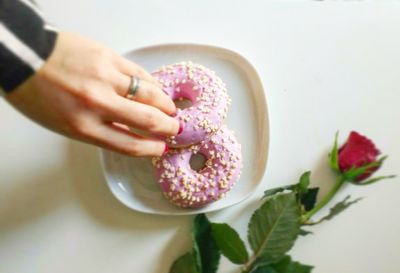 Cropped hand of woman holding donut in plate by rose on white table