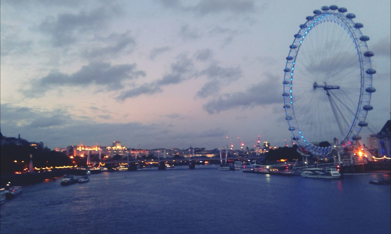 ferris wheel, amusement park, sky, amusement park ride, illuminated, arts culture and entertainment, built structure, water, architecture, night, cloud - sky, waterfront, building exterior, city, river, transportation, travel destinations, dusk, outdoors, travel