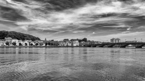 Arch bridge over river by buildings against sky