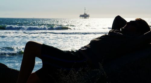 Man lying on rock at sea shore against sky