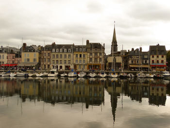 Sailboats moored on river by buildings against sky