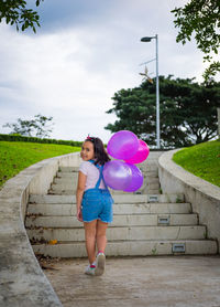 Portrait of happy girl with balloons climbing steps at park