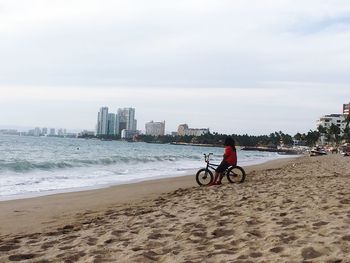 Man cycling on beach against sky