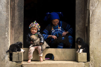 Portrait of smiling boy with dog by mother sitting at entrance