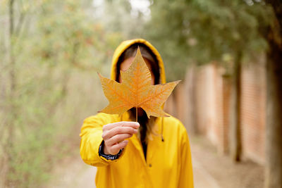 Woman holding autumn leaf in front of face
