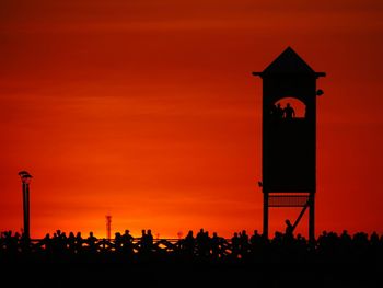 Silhouette people at beach against orange sky