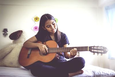 Teenage girl playing guitar on bed