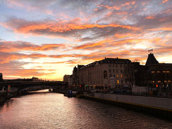 River amidst buildings against sky at sunset