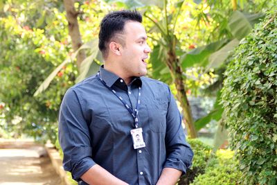 Young man looking away while standing against plants