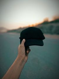 Midsection of person holding sea against sky during sunset