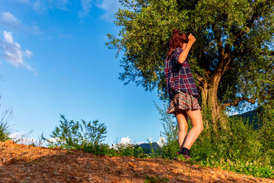 Woman standing by tree against blue sky