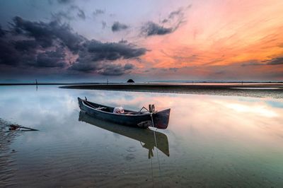 Boat moored on sea against sky during sunset