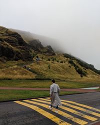 Rear view of woman walking on road against cloudy sky