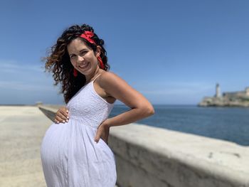 Side view of pregnant woman standing at the oceanside against sky