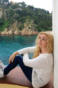 Portrait of young woman sitting by sea against sky