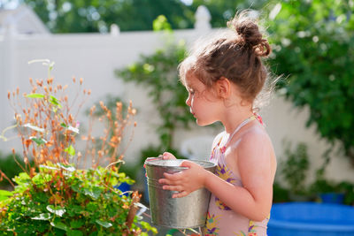 Cute young girl watering plants with a bucket on a summer day in the backyard