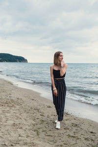 Rear view of woman standing at beach against sky