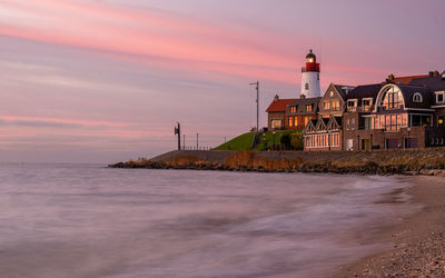 Lighthouse by sea against sky during sunset