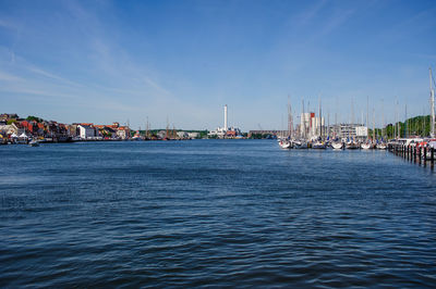 Sailboats moored on river in city against blue sky