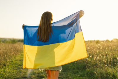 Ukrainian wonam in white t shirt with yellow and blue flag of ukraine in field.